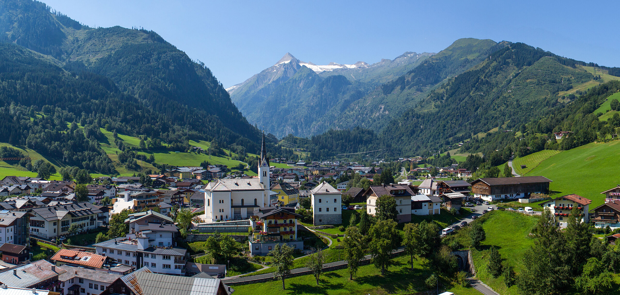 Dorf Kaprun mit Kirche, grünen Wiesen und schneebedeckten Gipfeln im Hintergrund