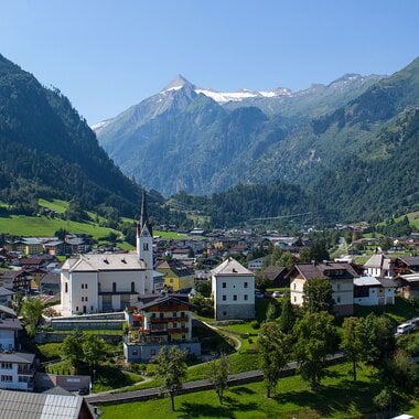 Dorf Kaprun mit Kirche, grünen Wiesen und schneebedeckten Gipfeln im Hintergrund
